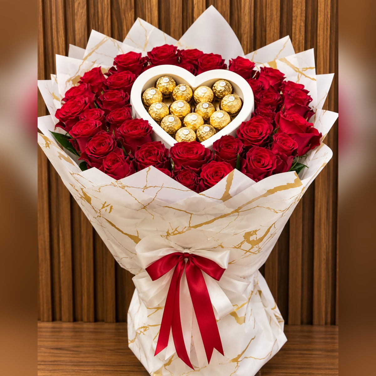50 roses rouges fraîches disposées autour d'un cœur de chocolats Ferrero Rocher, emballage blanc et doré